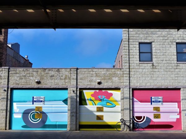 A tour bike leaning in front of three garage doors each painted in a different color with a third of a mural of a woman driving a car on each.