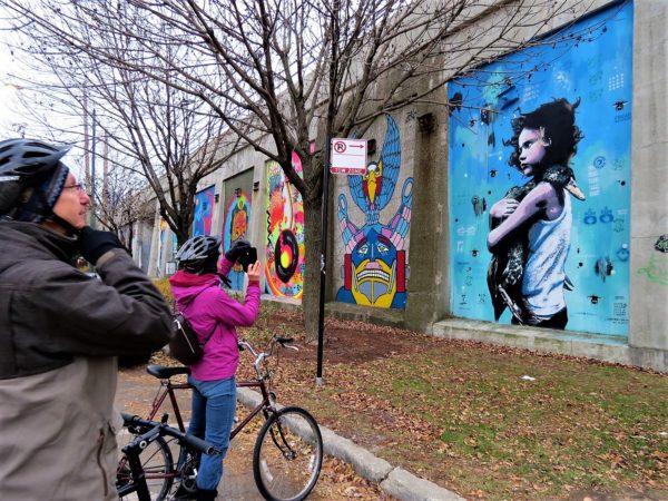 CBA bike tour riders taking a picture of a mural of a child holding a duck