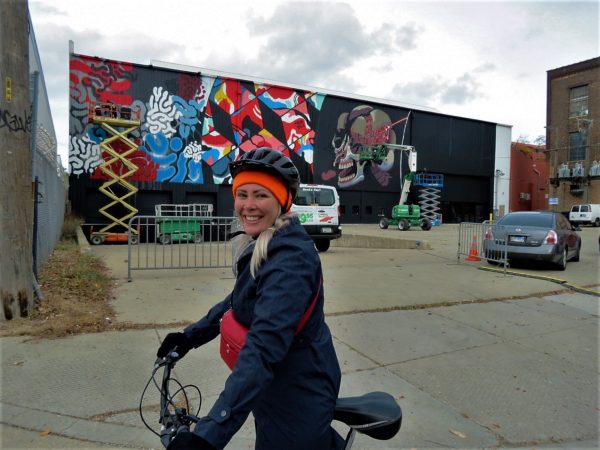 A CBA bike tour rider standing in front of street artists working on a large mural.