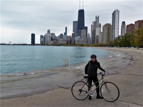 A CBA bike tour rider posing with the Chicago skyline and Lake Michigan behind.
