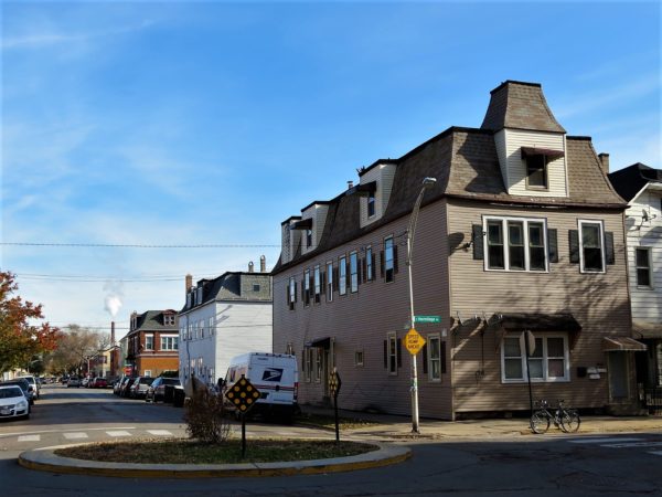 A tour bike leaning in front of an 1911 three story corner building with a mansard roof with two similar building extendin behind along the street.