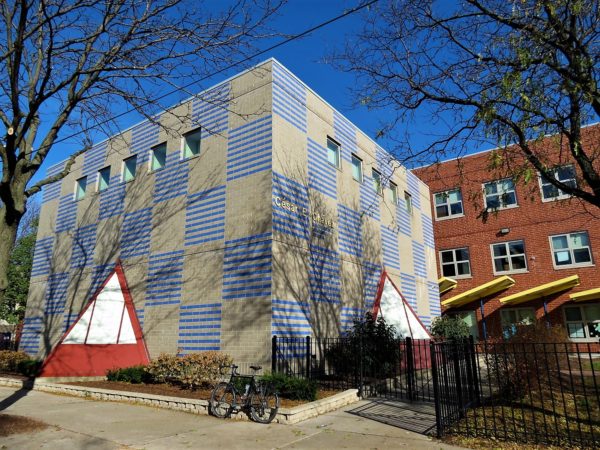 A tour bike leaning in front of a square structure painted with checkerboard blue and gray with a small red pyramid extension and three yellow entryway covers.