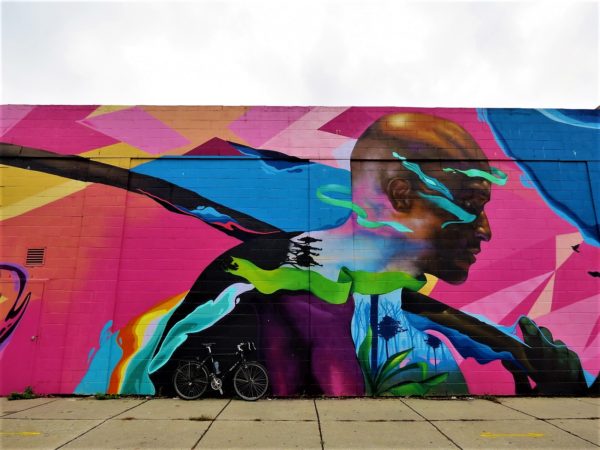A tour bike leaning on a bright multi-colored mural of a Black man with a samurai sword over his shoulder