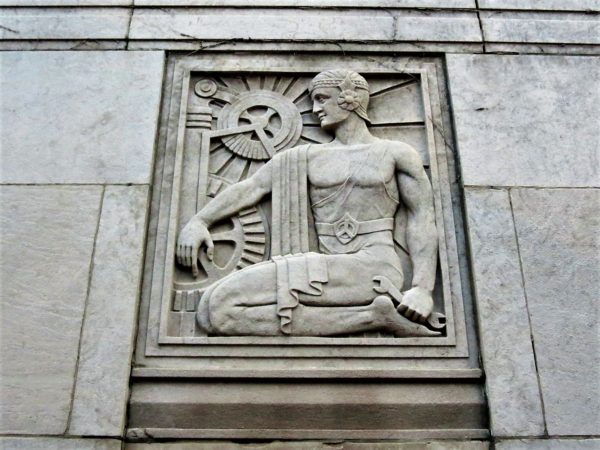A bas relief of a woman kneeling next to machinery