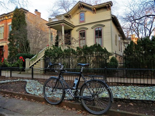 A tour bike standing in front of a one and half story Italianate house
