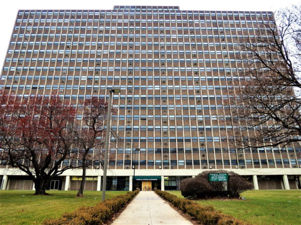 A tour bicycle leaning on the boarded front of multistory brown brick and glass apartment block that fills the photo.