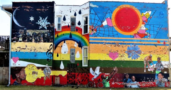 A tour bike leaning on a mural of a red sun, rainbow, and a snowy night sky