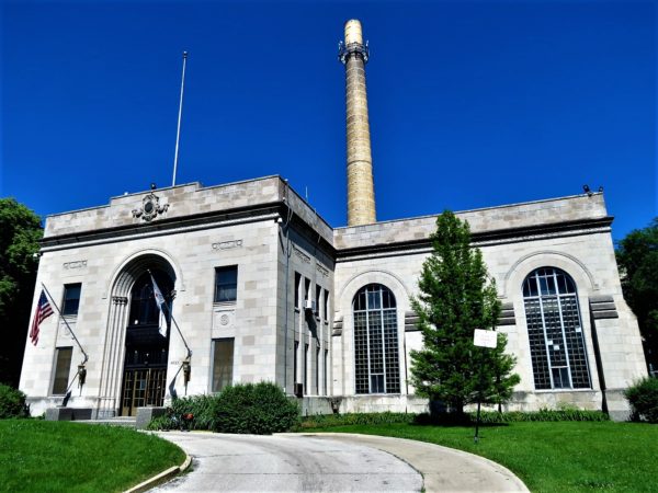 A tour bicycle standing in front of a bright white stone industrial building with a center chimney.