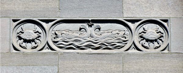A white stone details of two crabs on either side of two whales or fish floating in water tail to tail