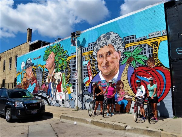 CBA bike tour riders posing in front of a mural of Logan Square iconic people, buildings, and events.