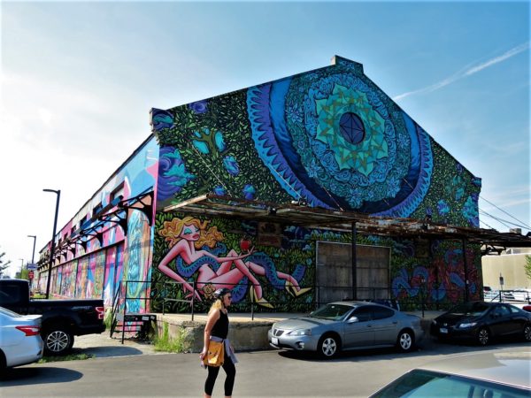 A CBA bike tour rider looking at a former railroad warehouse covered in murals of different ages