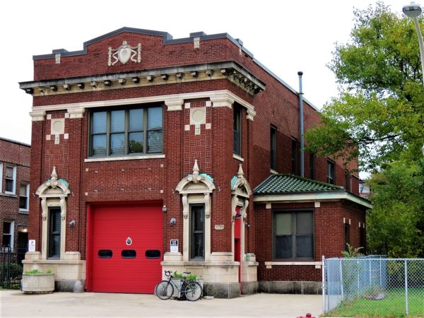 A tour bicycle leaning on a red brick former firehouse with single red bay and cornice and white stone design details