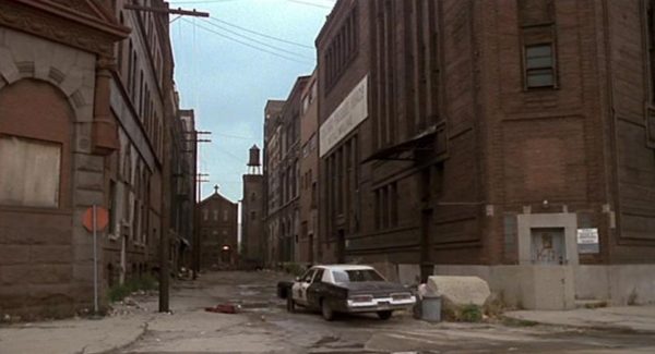 Movie still of the Blues Brothers bluemobile driving between two brick buildings