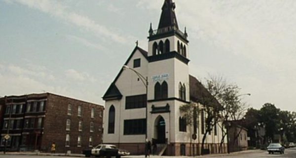 A Blues Brothers movie still of a white and dark brown wood church with the Bluesmobile parked in front.