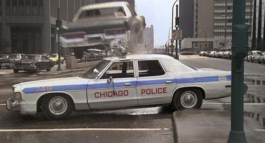 A Blues Brothers movie still of the Bluesmobile jumping over a police car.