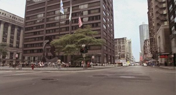 A Blues Brothers first person POV of a street intersection with a brown metal baboon like Picasso statue in the background,