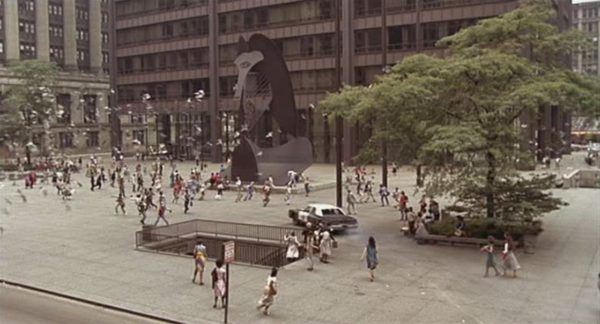 A Blues Brothers movie sill of the Bluesmobile moving across a pedestrian square with pedestrians scattering