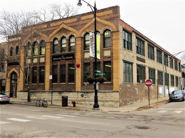 A tour bike standing in front of a two story brick industrial building with a detailed tan and brown brick design facade