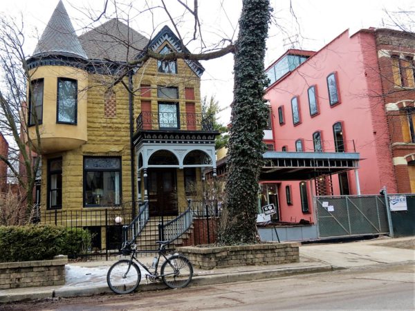 A tour bicycle standing in front of a yellow limestone two story Queen Anne home with a wooden entry porch
