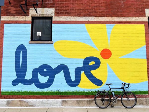 A tour bike leaning on a blue background mural wirh love in cursive and a yellow red centered flower 