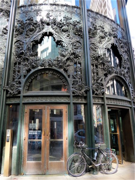 A tour bike leaning on the black metal organic pattern building entrance of the Carson Pirie Scott Building