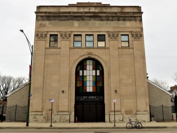 A tour bike standing in front of a limestone three story Classical Revival former bank with a white cross in the large arched middle window.