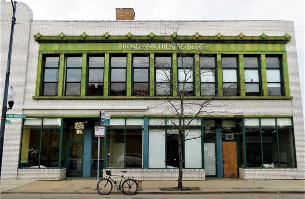 A tour bicycle standing in front of a white brick Art Moderne two story theater building with fist floor retail and green terra cotta framed second floor windows