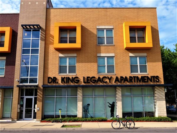 A tour bike standing in front of a modern tan three story apartment tan brick and glass building with yellow extended square window sills