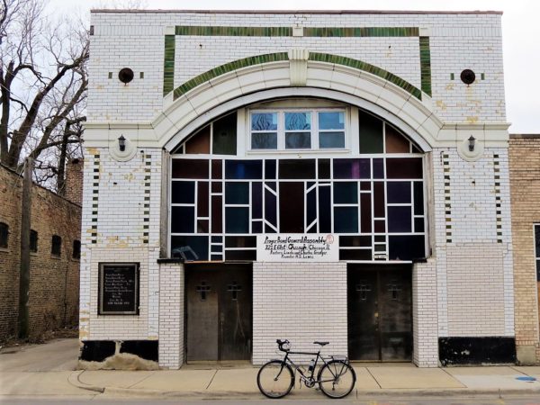 A tour bike standing in front of a green and white glazed brick two story with an arched modern colored glass front window