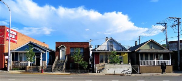 A tour bike standing in front of four one story raised residences with walk up stairs to the front door.