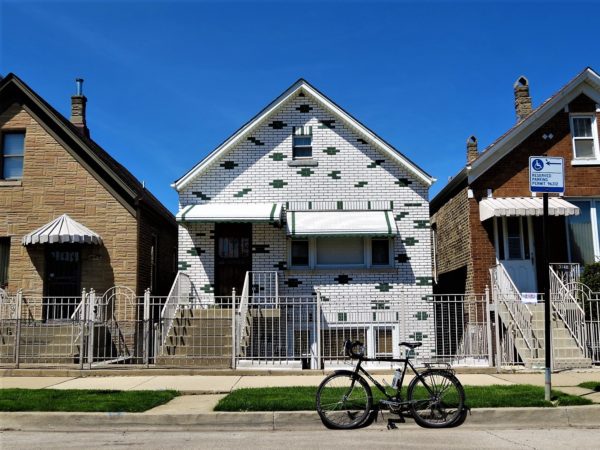 A tour bike standing in front of a one and half story worker's cottage clad in green and white glazed brick