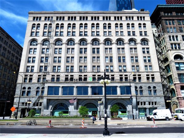 A tour bike standing in the street in front of a late 19th century heavy massed 12 story granite building with a triple arched enry and an arched window seventh floor.