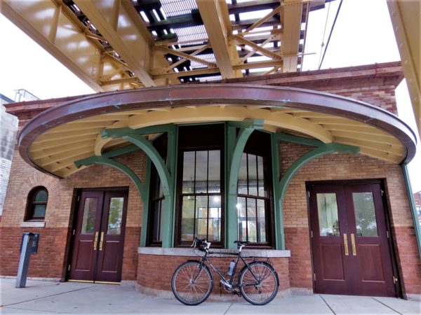 A tour bike leaning on the front of a early 1890s elevated train station with a broad circular roof.