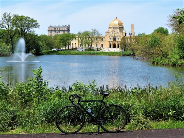 A tour bike standing in front of a lagoon with fountain and a golden domed building in the near distance.