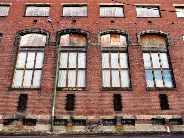 A tour bike standing in front of a red brick three story with four boarded tall vertical limestone arched windows and matching square windows above.