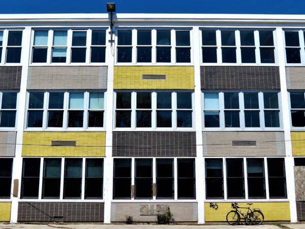 a tour bike leaning on a black, grey, and yellow glazed brick between vertical windows of a  Mid Century Modern three story school.