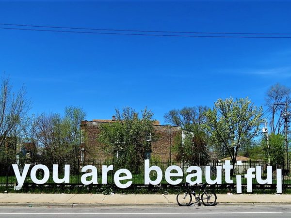 A tour bike standing on the road in fornt of a typeface installation that reads You are beautiful with park trees and a deep blue sky behind.