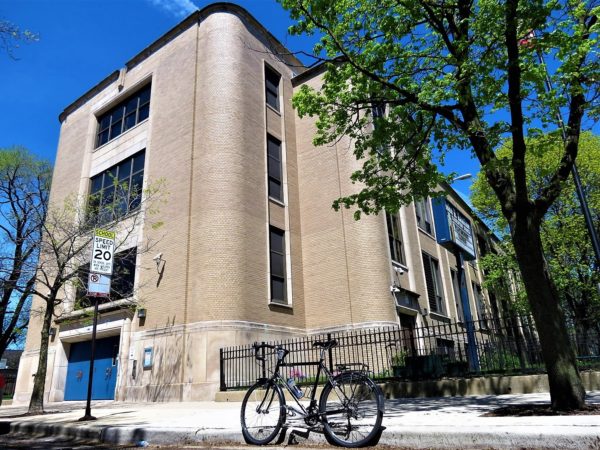 A tour bike standing to the side of an Art Moderne four story tan brick elementary school building.