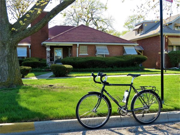 A tour bike at the curb with a Midcentury Ranch style home in the background