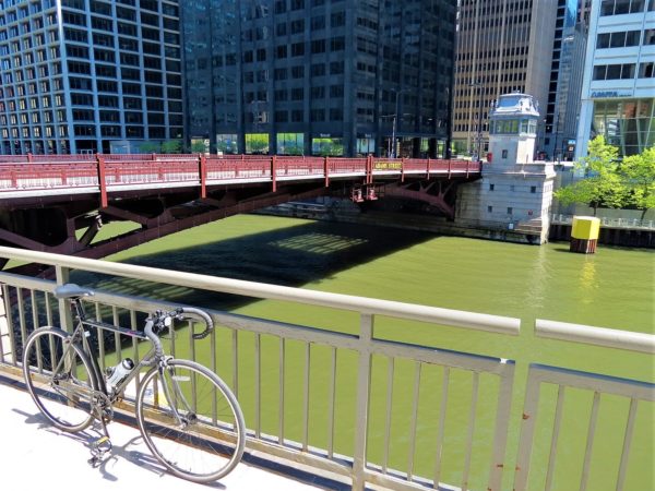 A tour bike leaning in the foreground with a rail height maroon movable bridge with bronze topped minder house at the far end.