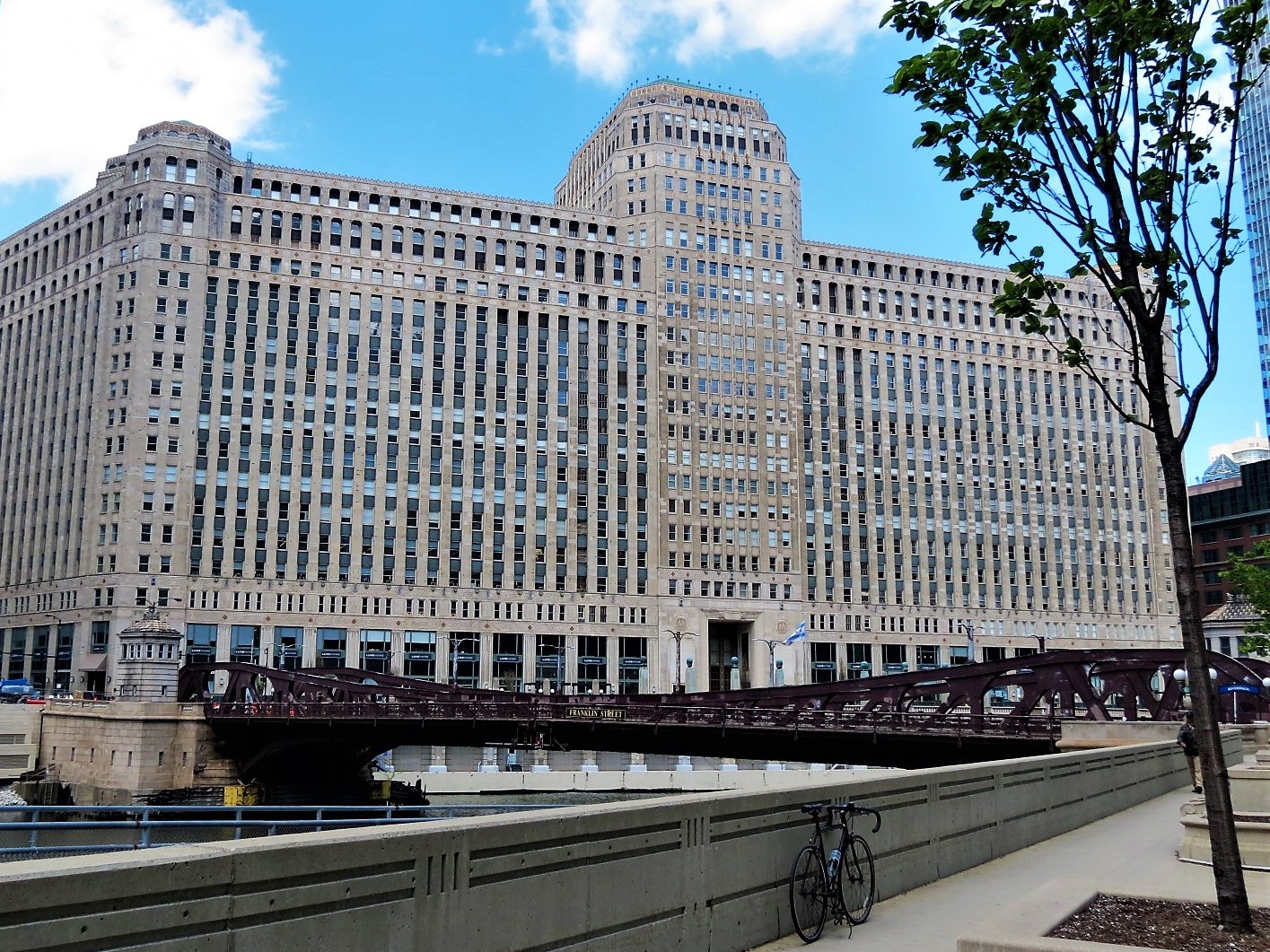 A tour bike leaning on a concrete planter with a maroon painted pony truss movable bridge and a massive Art Deco building in the background