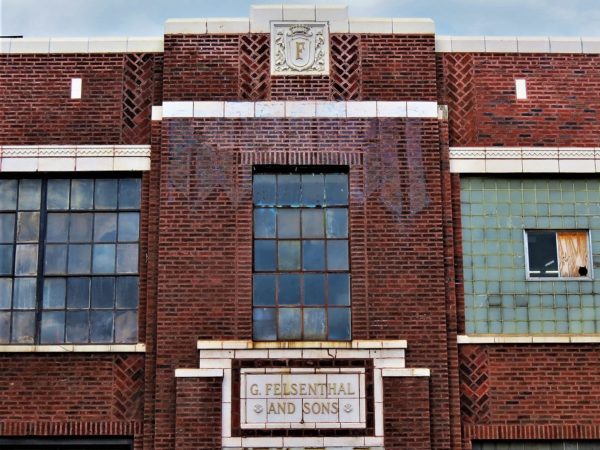White terra cotta business insignia and name plate  on a red brick building with small paneled industrial windows.