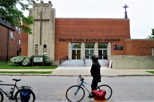 A CBA bike tour rider looking at an Arc Deco stone and brown brick church.