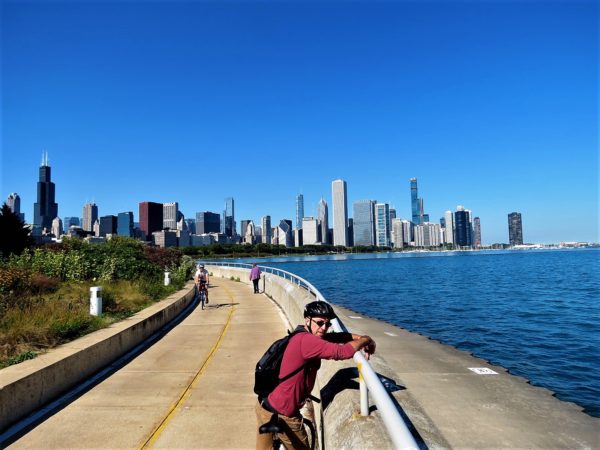 A CBA bike tour rider leaning on a railing above the lake with the Chicago skyline in the background.