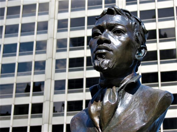 A bronze bust of a shaggy haired black man in late 18th Century coat and ruffle.