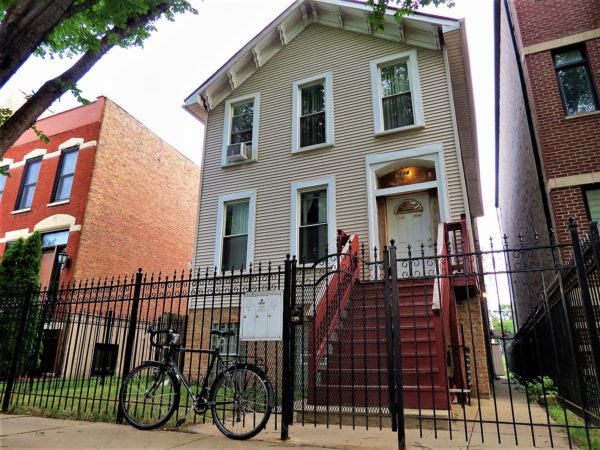 A tour bike leaning on the black metal fence in front of an angled roof wooden Italianate two story home.