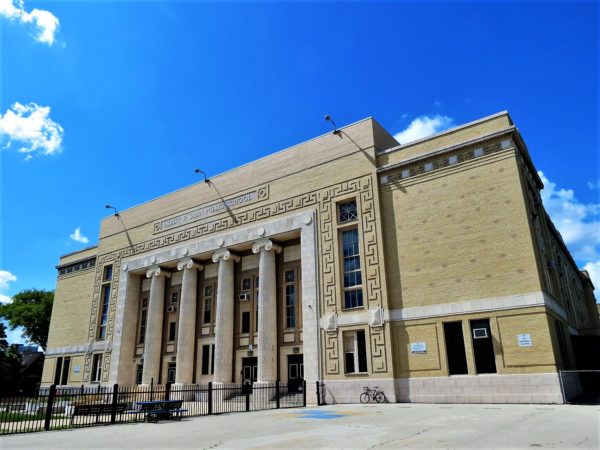 A tour bike leaning on a yellow brick patterned Classical Revival limestone column main entrance school building.