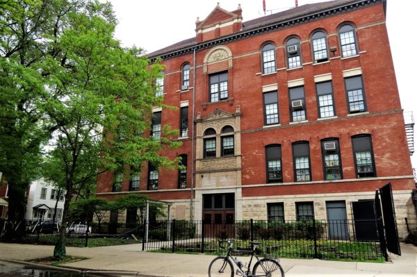 A tour bike standing in front of a red brick and limestone detailed Queen Anne four story elementary