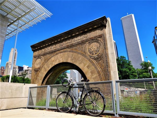 A tour bike in front of botanic motif terra cotta arch with a white marble skyscraper in the background.