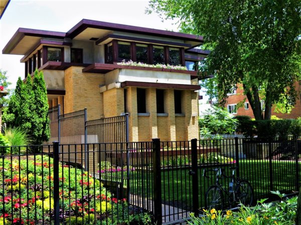 A tour bike leaning a the black metal fence around a three story Prairie Style wood and yellow brick home.